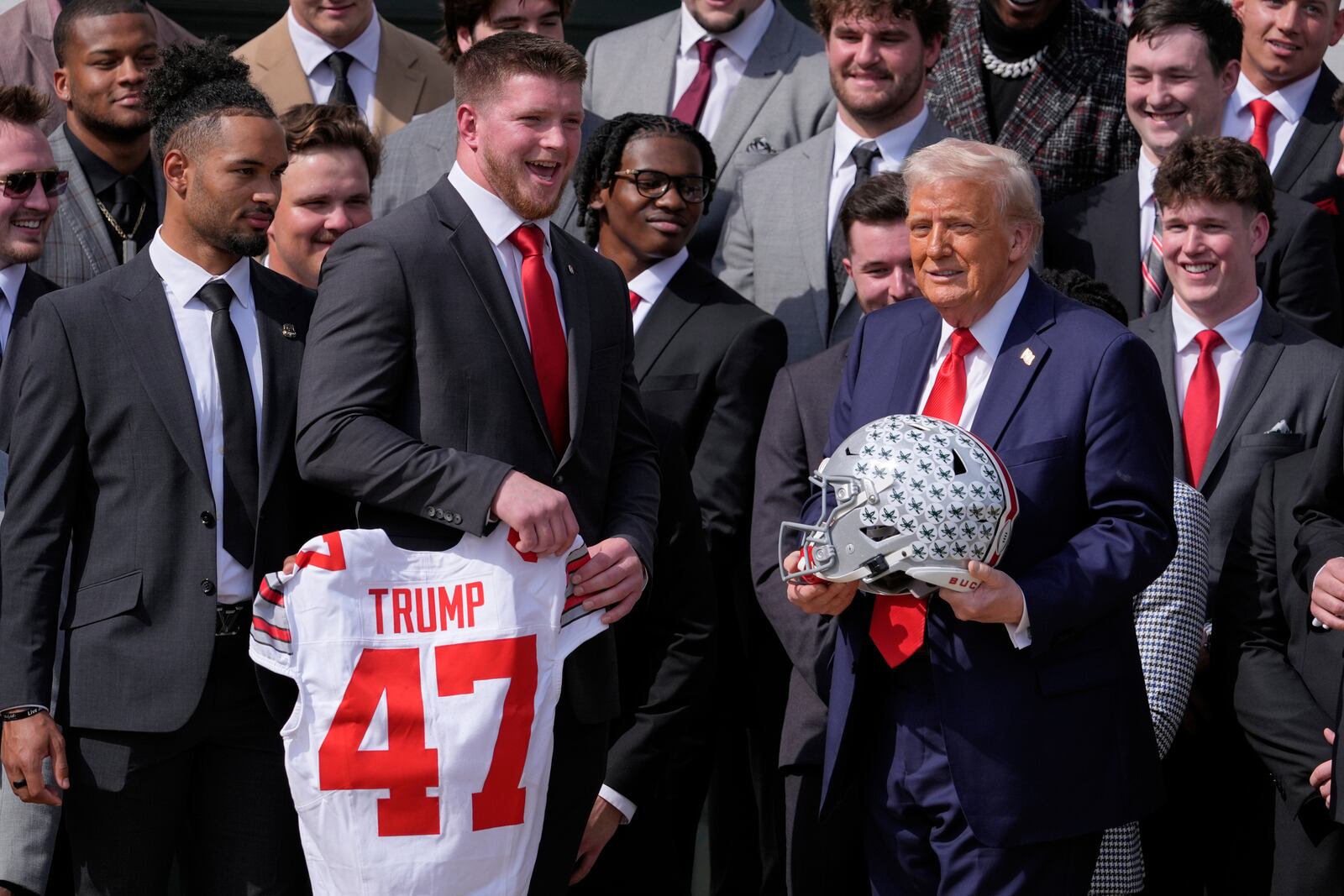 President Donald Trump, right, holds a helmet while standing near a jersey gifted by the Ohio State University football team as Trump welcomes the 2025 College Football National Champions during an event on the South Lawn of the White House, Monday, April 14, 2025, in Washington. (AP Photo/Manuel Balce Ceneta)