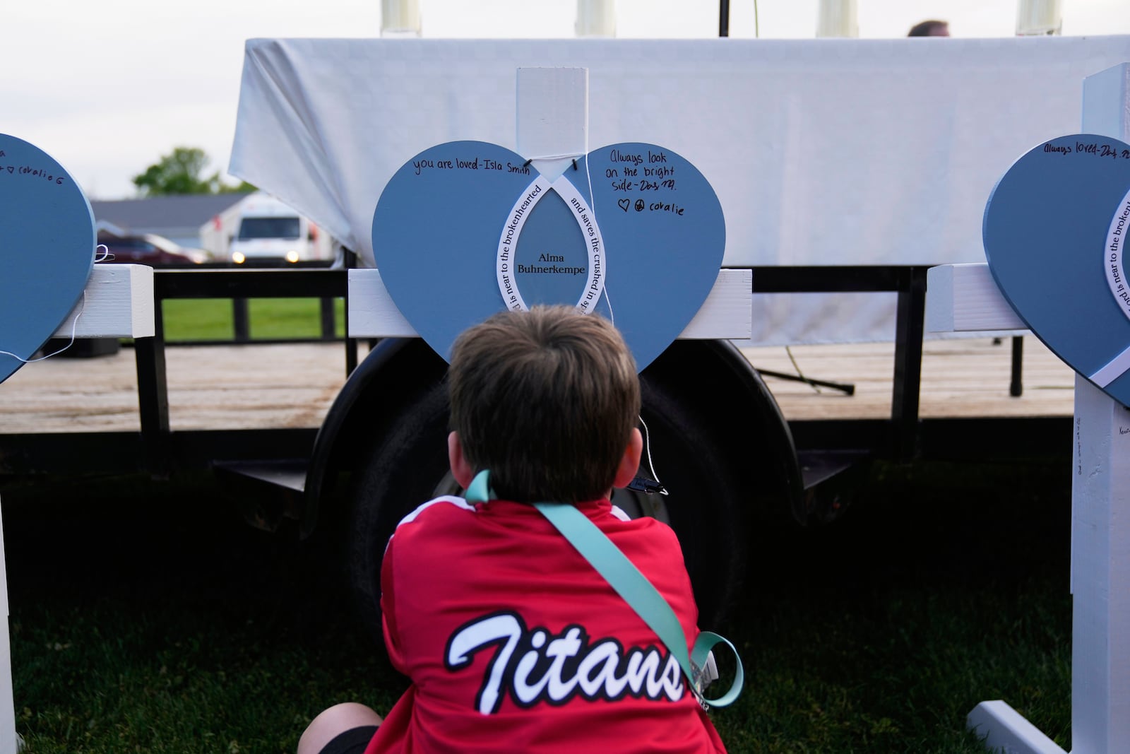 Seven-year-old Harriet Glessner writes on a heart for Alma Buhnerkempe at a vigil for three young children and a teenager, including Buhnerkempe, who were killed when a car barreled through a building used for an after-school camp Tuesday, April 29, 2025, in Chatham, Ill. (AP Photo/Erin Hooley)