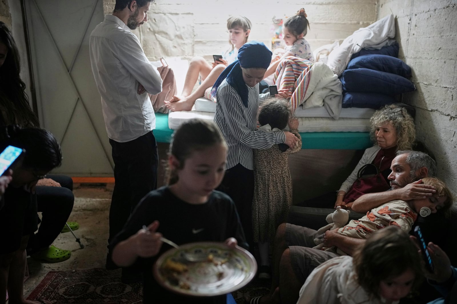 Israelis take shelter in a basement as a siren sounds a warning following missile launches from Iran, in Jerusalem, Sunday, June 15, 2025. (AP Photo/Ohad Zwigenberg)