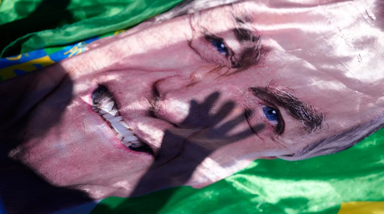 The shadow of a supporter of former President Jair Bolsonaro is cast on an image of him displayed outside the hospital where he was transported from prison for surgery the next day, in Brasilia, Brazil, Wednesday, Dec. 24, 2025. (AP Photo/Eraldo Peres)