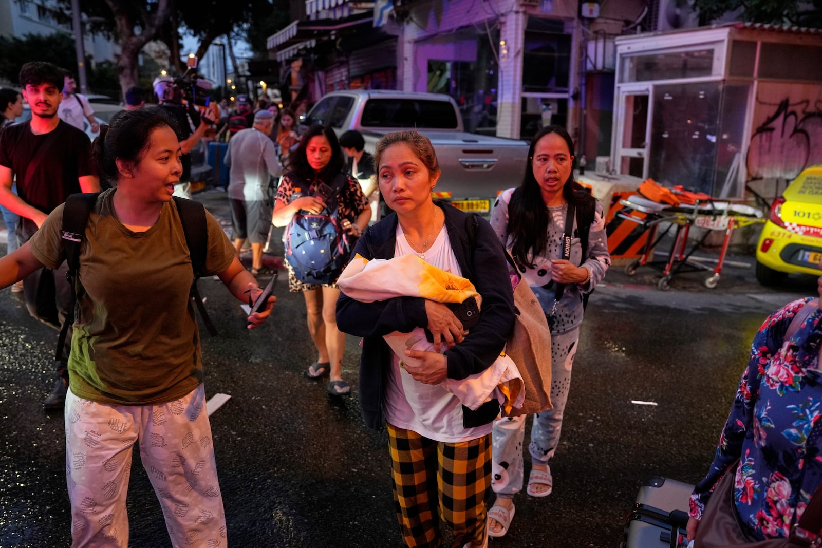 A woman holds her baby as residents evacuate the area after a missile launched from Iran struck in downtown Tel Aviv, Israel, Monday June 16, 2025. (AP Photo/Baz Ratner)
