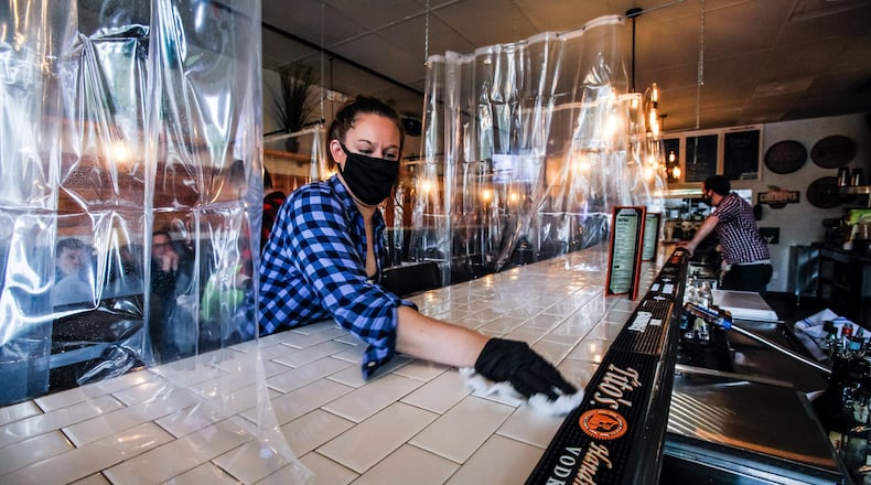 Arlene Williams cleans the bar at Bourbon’s Craft Kitchen & Bar on the first day back for dining in at restaurants in over two months Thursday, May 21, 2020 at Bourbon’s Craft Kitchen & Bar in Middletown. Bourbon’s Craft Kitchen & Bar installed clear shower curtains to seperate diners and is cleaning tables and curtains in between visitors to comply with guidelines during the coronavirus pandemic. NICK GRAHAM /STAFF
