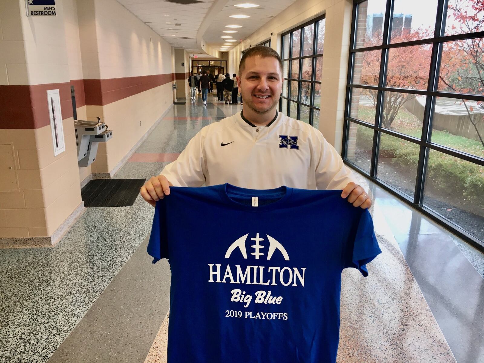 Hamilton High School Interim Athletic Director Tyler Belew shows off one of the special football playoff T-Shirts the Butler County school has printed up prior to tonight’s historic game against neighboring Fairfield High School. The two Greater Miami Conference (GMC) rivals have never played before in the state playoffs and Hamilton hasn’t qualified for the playoffs since 2010. (Photo By Michael D. Clark/Journal-News)