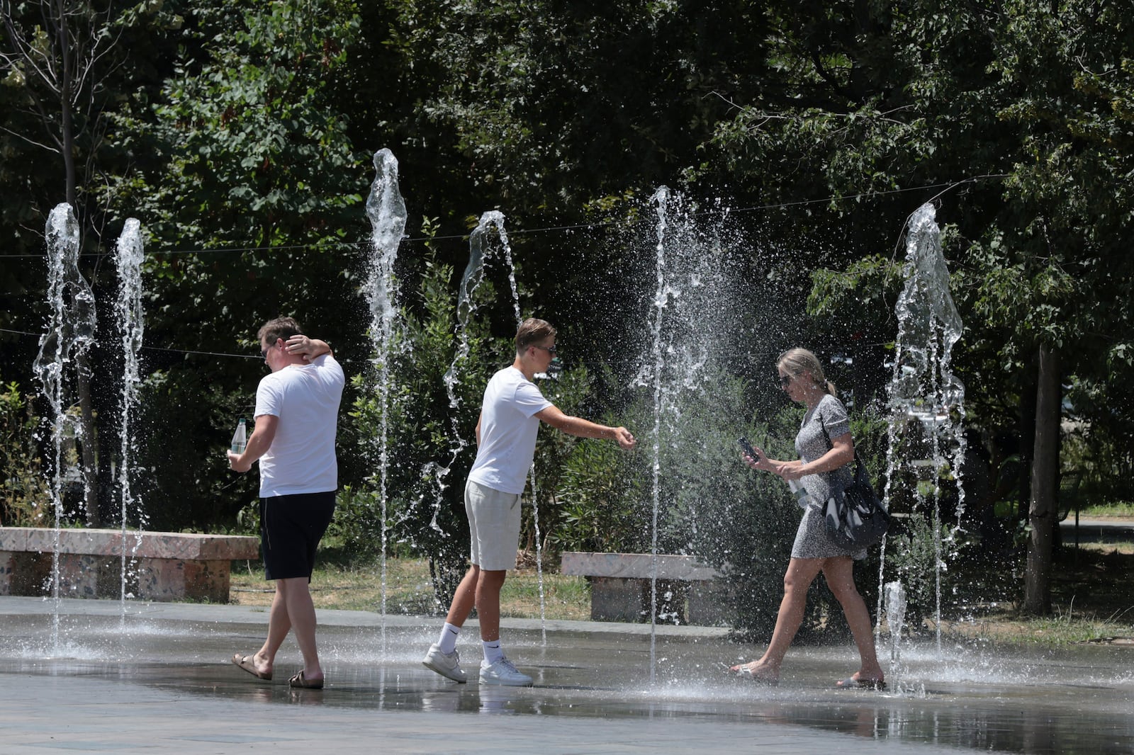 Pedestrians cool themselves in a fountain in central Tirana, Albania, during a heatwave on Friday, July 25, 2025. (AP Photo/Vlasov Sulaj)