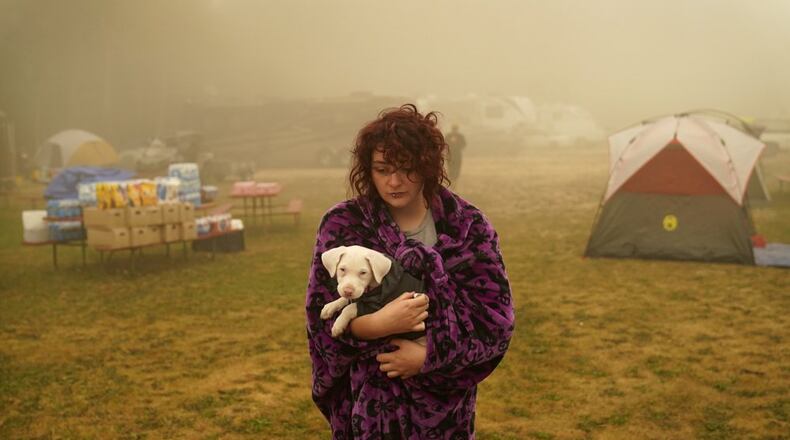 Shayanne Summers holds her dog Toph while wrapped in a blanket after several days of staying in a tent at an evacuation center at the Milwaukie-Portland Elks Lodge, Sunday, Sept. 13, 2020, in Oak Grove, Ore. "It's nice enough here you could almost think of this as camping and forget everything else, almost," said Summers about staying at the center after evacuating from near Molalla, Oregon which was threatened by the Riverside Fire. (AP Photo/John Locher)