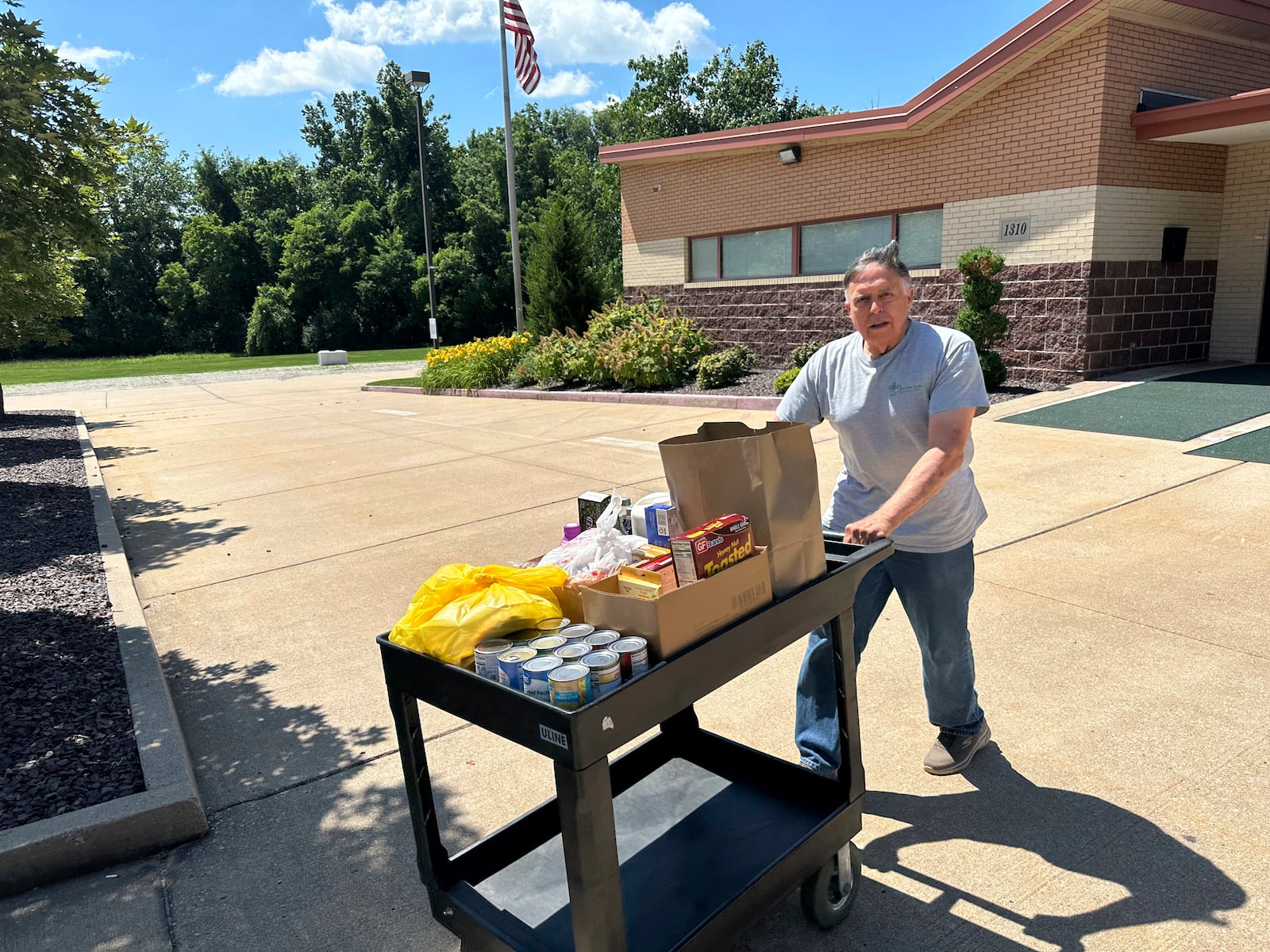 Dick Hronick, a volunteer at the Samaritan Center food pantry in Jefferson City, Mo., pushes a cart of food across the parking lot for distribution to people on Tuesday, July 1, 2025. (AP Photo/David A. Lieb)