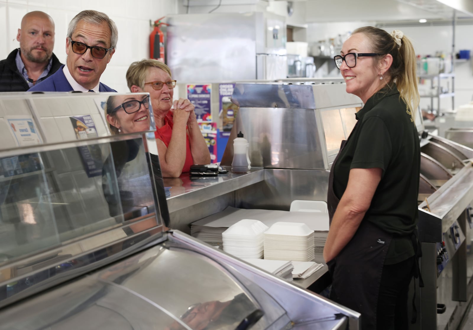 Reform UK leader Nigel Farage speaks to a woman behind the counter of a fish and chip shop as he campaigns with Reform UK mayoral candidate Andrea Jenkyns in Scunthorpe, England, Tuesday, April 29, 2025. (AP Photo/Darren Staples)