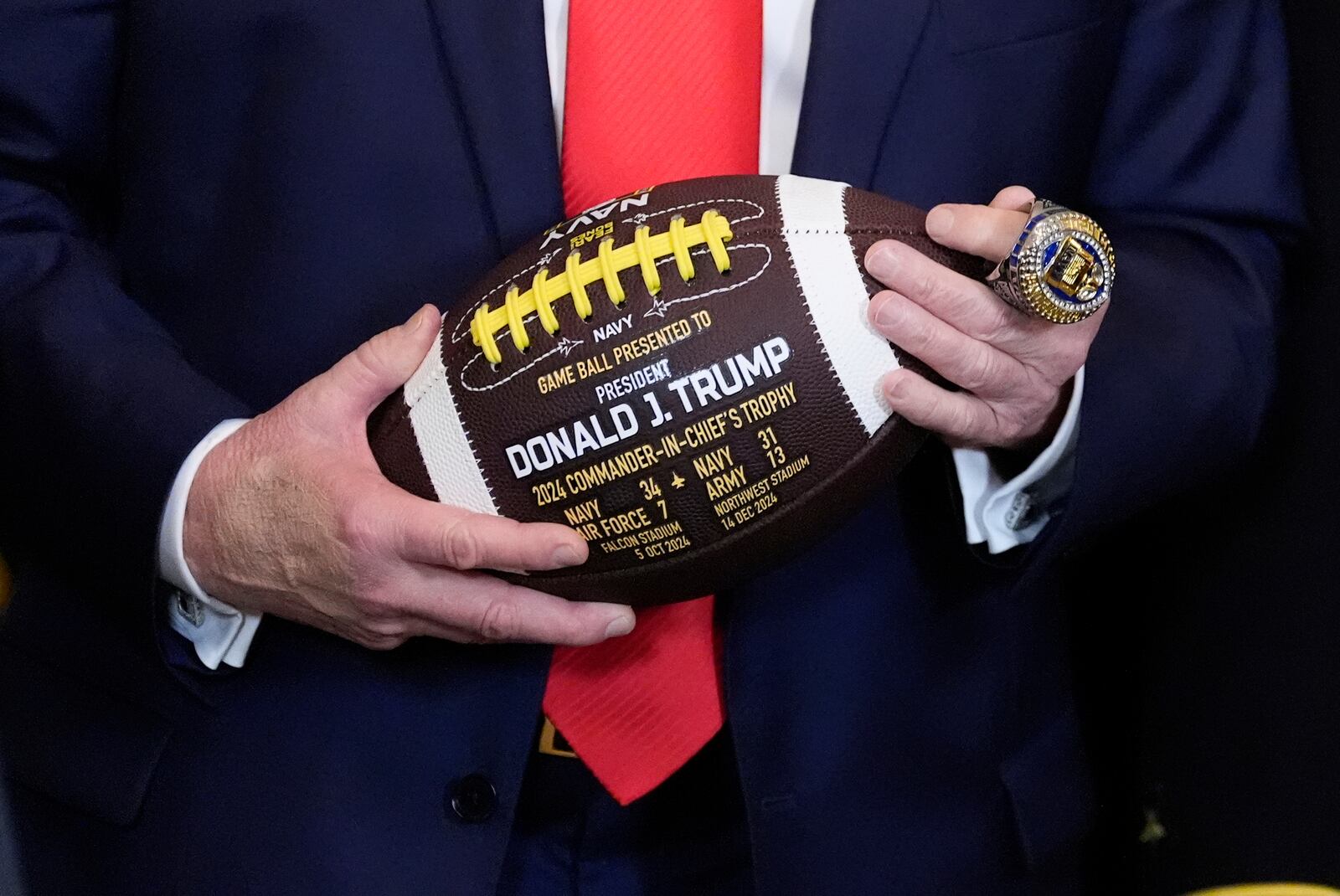 President Donald Trump holds a football and wears a ring presented to him during the Commander-in-Chief trophy presentation to the Navy Midshipman football team in the East Room of the White House, Tuesday, April 15, 2025, in Washington. (AP Photo/Alex Brandon)