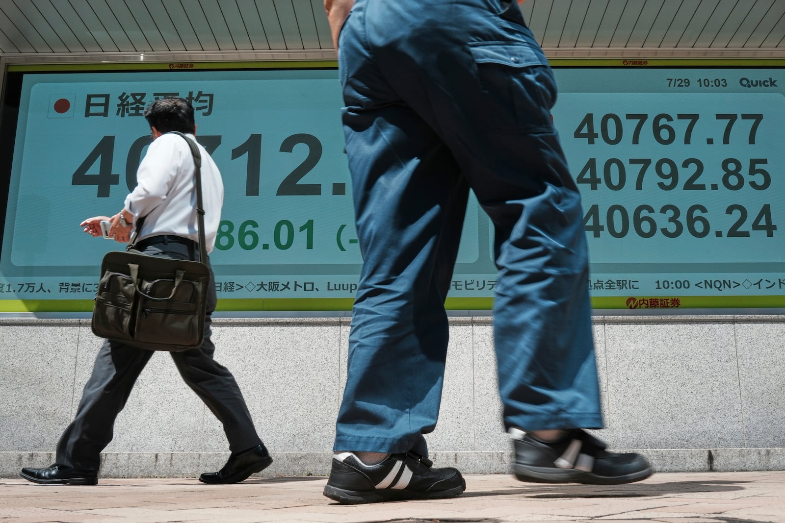 Persons walk in front of an electronic stock board showing Japan's Nikkei index at a securities firm Tuesday, July 29, 2025, in Tokyo. (AP Photo/Eugene Hoshiko)