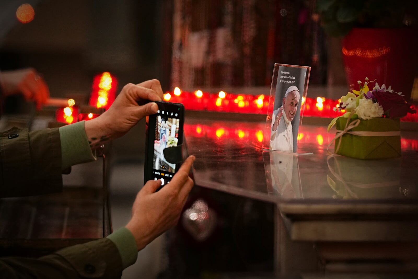 A woman takes a picture of a photograph of the late Pope Francis, that reads "Please, don't forget to pray for me" during a mass in his memory at the Chiesa di Santo Spirito in Sassia outside the Vatican, Thursday, April 24, 2025. (AP Photo/Andreea Alexandru)