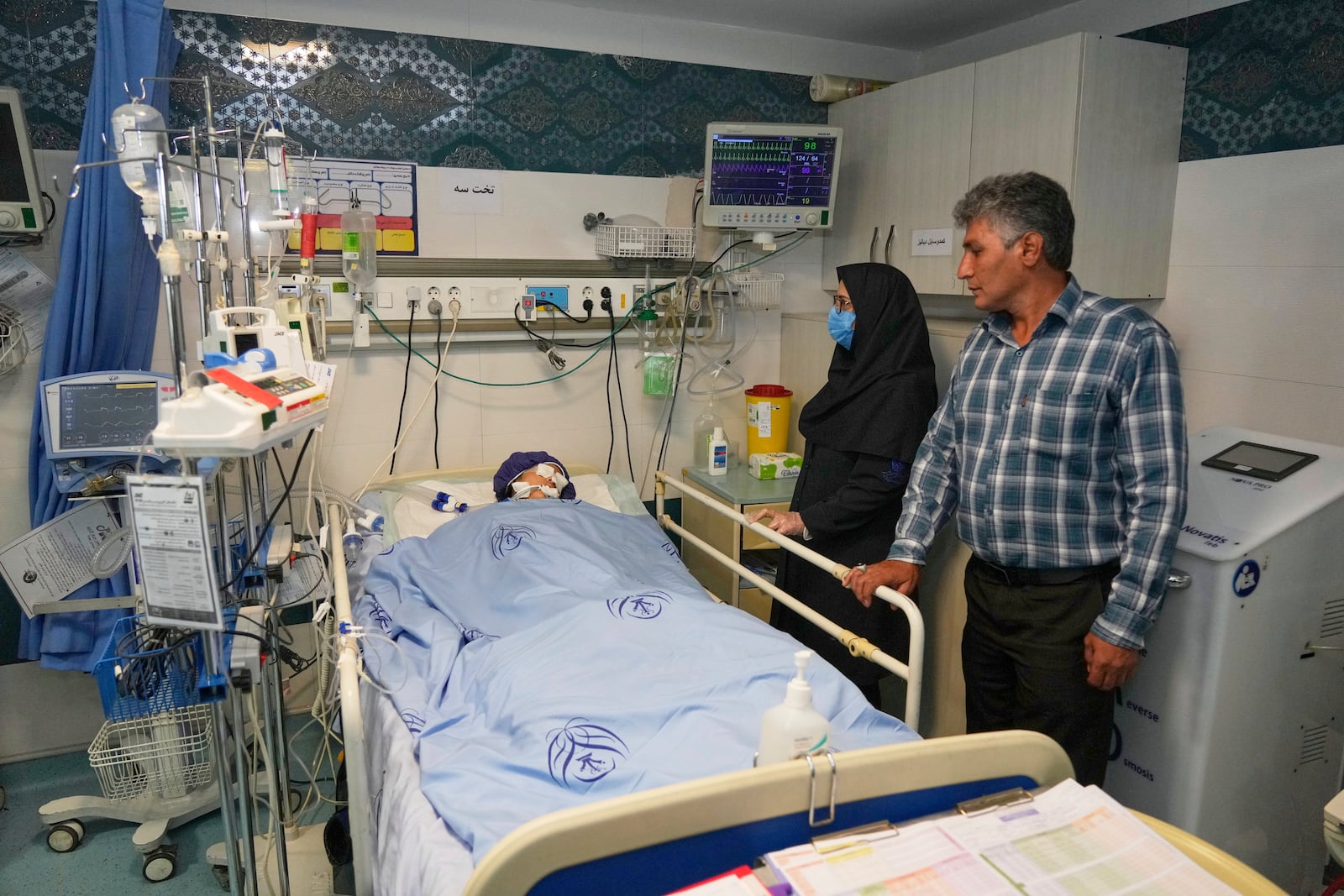 Parnia Rahmanian, 13, lies unconscious in a hospital bed following Israeli strike that targeted her neighborhood, as a nurse, second right, and a relative look on, in Tehran, Iran, Saturday, June 21, 2025. (AP Photo/Vahid Salemi)