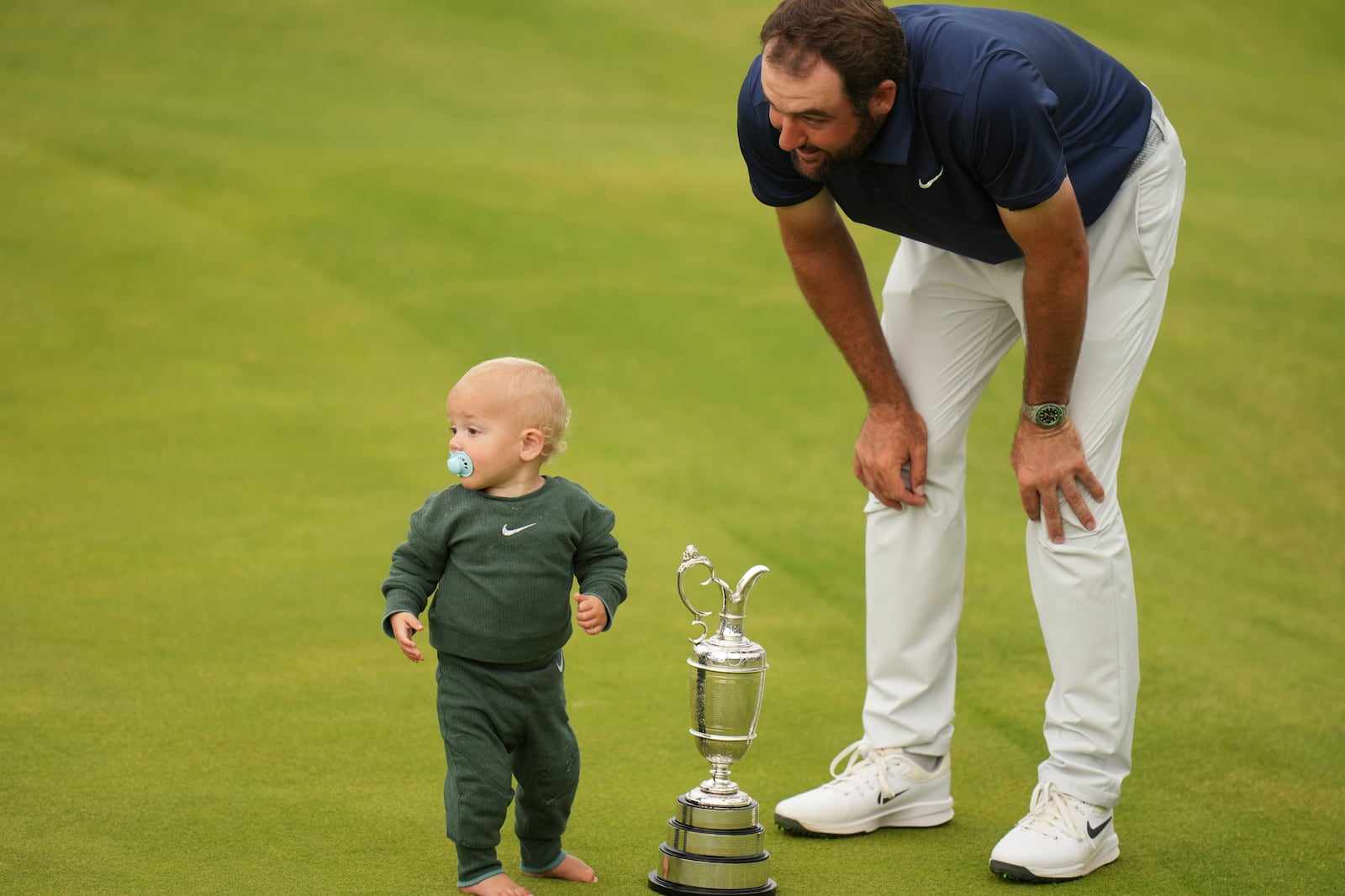 Scottie Scheffler of the United States with his son Bennett as he poses for photographers with the Claret Jug trophy after winning the British Open golf championship at the Royal Portrush Golf Club, Northern Ireland, Sunday, July 20, 2025. (AP Photo/Francisco Seco)