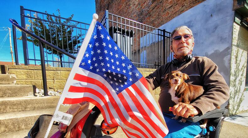 Paul Tunstall holds his dog, Daisy, as he cruises down the sidewalk along Main Street on his electric scooter carrying an American flag on election day Tuesday, Nov. 3, 2020 in Hamilton. Tunstall voted early but was still showing his support to voters on election day with the flag. NICK GRAHAM / STAFF