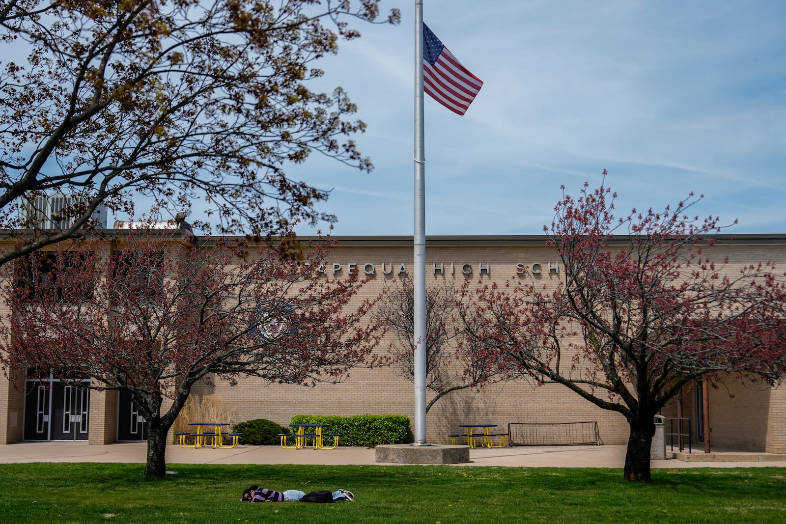 A person lies on the grass in front of Massapequa High School, in Massapequa, N.Y., Friday, April 25, 2025. (AP Photo/Julia Demaree Nikhinson)