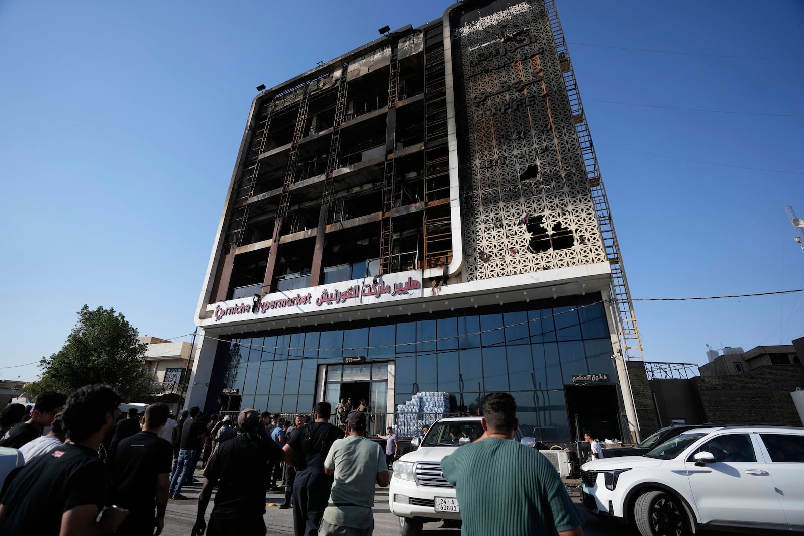 Iraqi people gather in front of a burning hypermarket building in Kut, Iraq, Thursday, July 17, 2025. (AP Photo/Hadi Mizban)