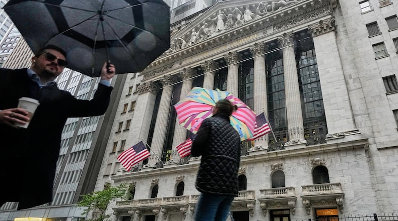 People with umbrellas pass the New York Stock Exchange, Monday, Oct. 13, 2025. (AP Photo/Richard Drew)