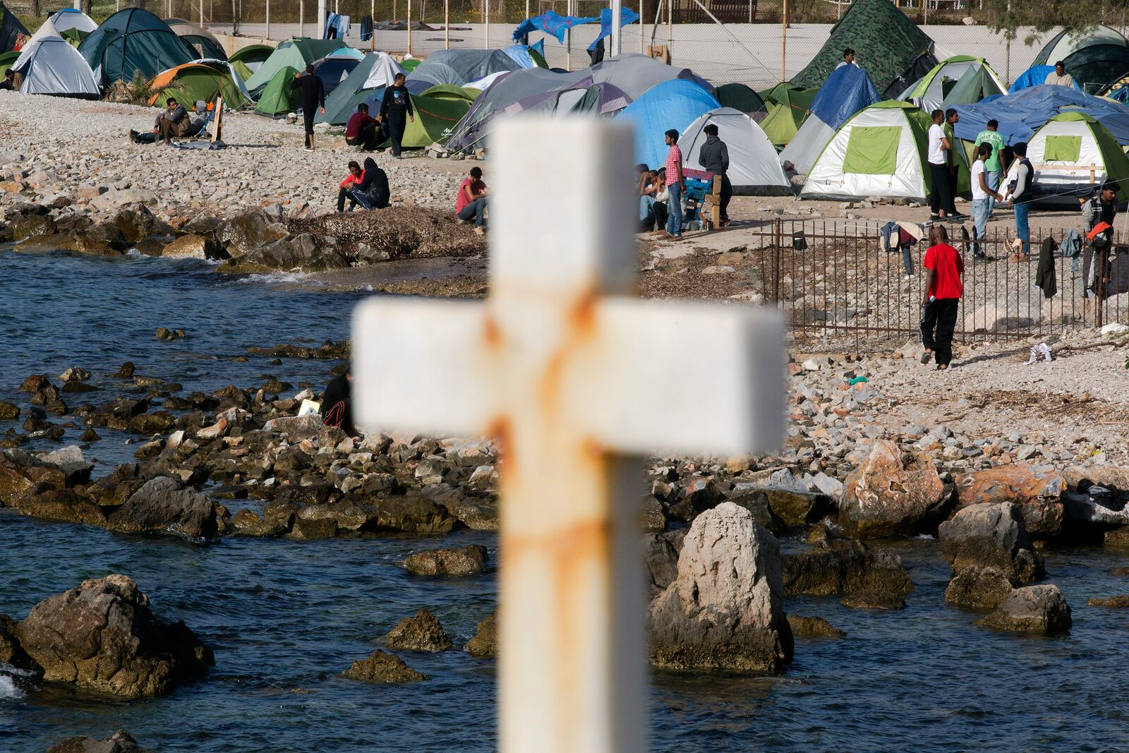 FILE - Migrants and refugees walk behind a cross in a camp set up by volunteers near the port of Mytilini, on the Greek island of Lesbos, April 15, 2016. (AP Photo/Petros Giannakouris, File)