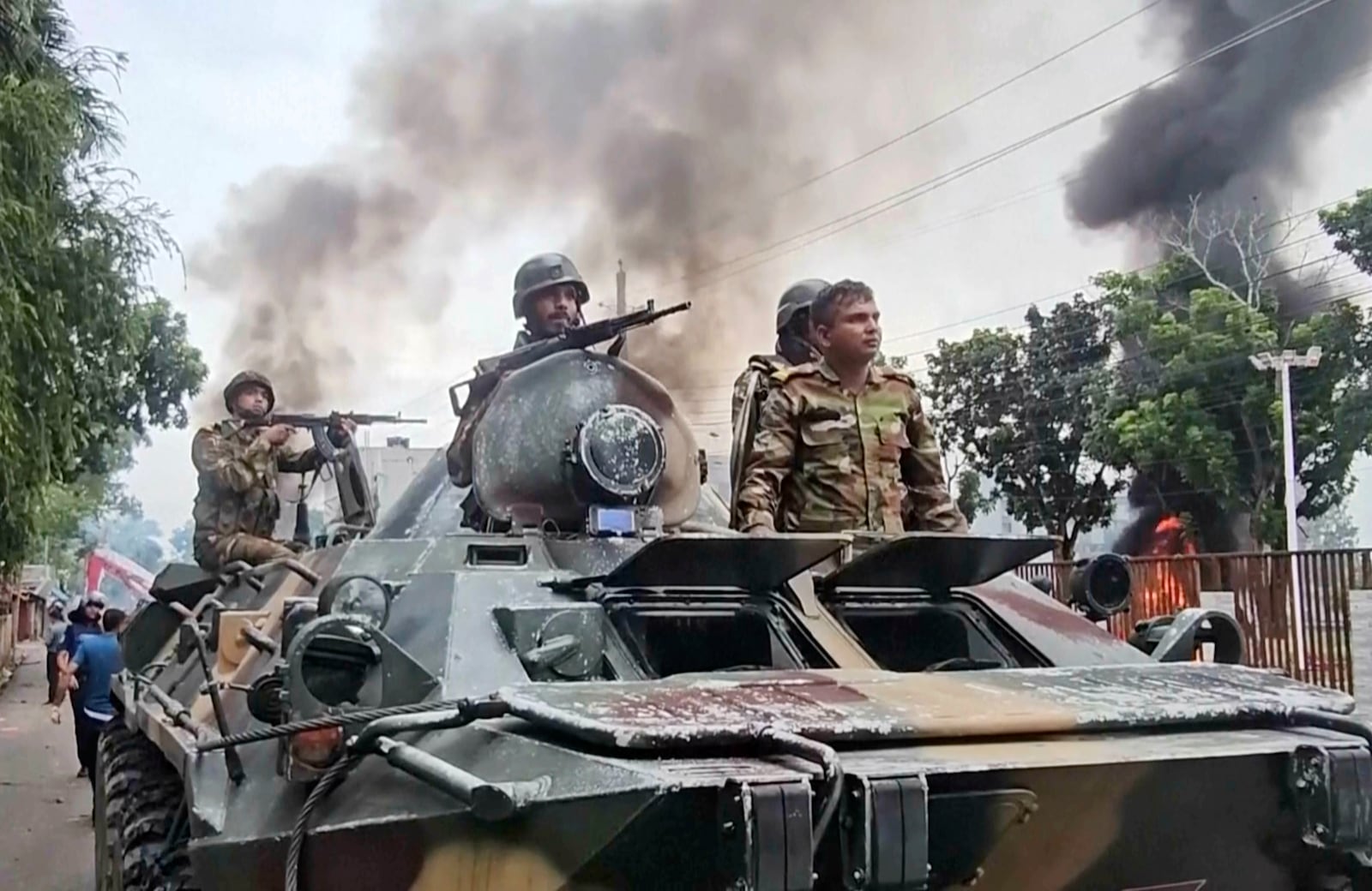 In this image made from a video, smoke rises behind an armored vehicle as supporters of the ousted Prime Minister Sheikh Hasina clash with security forces in Gopalganj, Bangladesh, Wednesday, July 16, 2025. (AP Photo)