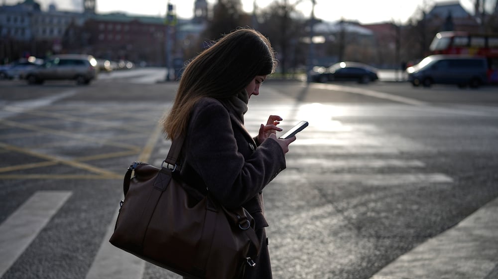A woman looks at her smartphone in central Moscow, Russia, Thursday, Nov. 20, 2025. (AP Photo/Alexander Zemlianichenko)