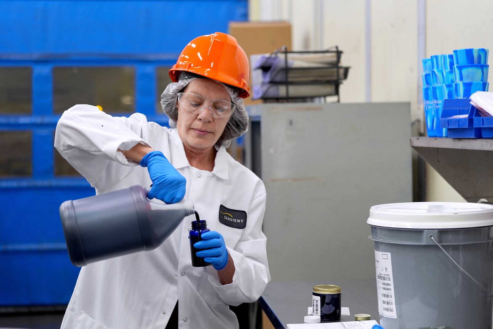 Technician Heather Browning pours a liquid color sample into a smaller container to be shipped to a customer at Sensient Technologies Corp., a color additive manufacturing company, in St. Louis., on Wednesday, April 2, 2025. (AP Photo/Jeff Roberson)