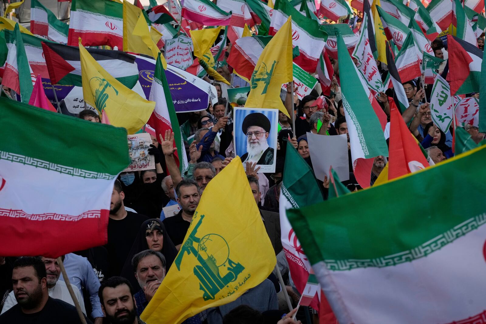 Demonstrators wave Iranian and Hezbollah flags as one holds up a poster of Iran's Supreme Leader Ayatollah Ali Khamenei during a rally marking the Muslim Shiite holiday of Eid al-Ghadir, which commemorates the Prophet Muhammad naming his successor, Ali, who is revered as the first Shiite imam, in Tehran, Iran, Saturday, June 14, 2025. (AP Photo/Vahid Salemi)