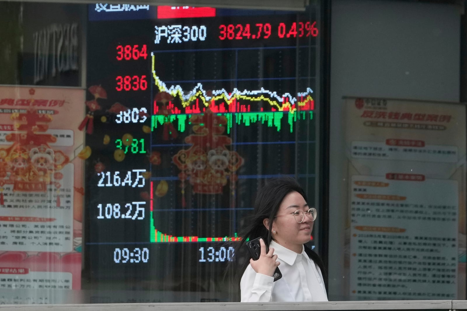 A woman passes by a stock index at a brokerage in Beijing, Wednesday, May 7, 2025. (AP Photo/Ng Han Guan)