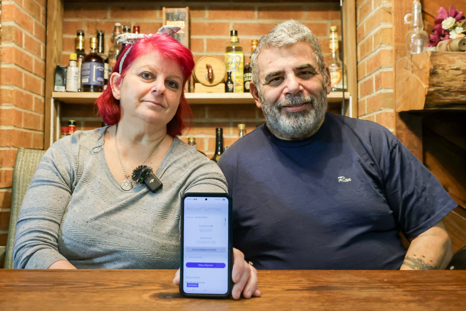 Mindi and Ron Wynne pose with a nearly $940 electric bill from AES Ohio displayed on her cell phone at their Perry Township home on Friday, Feb. 20. “Life doesn’t need to be free. Let’s just be fair,” Mindi said. “Give people a chance to catch up on things.” BRYANT BILLING / STAFF PHOTO ILLUSTRATION