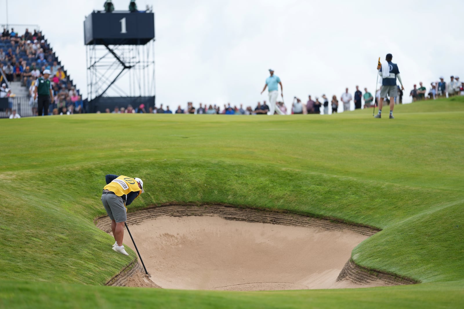 Jason Reynolds caddie for Dean Burmester of South Africa of South Africa, rakes a bunker on the 1st after Burmester played a shot from it during the third round of the British Open golf championship at the Royal Portrush Golf Club, Northern Ireland, Saturday, July 19, 2025. (AP Photo/Jon Super)