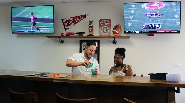 Brenton Semplak, from the Waterford's therapy team, served as bar tender for the grand opening of the sports bar at the Waterford of Fairfield. Activities director Alexis Jenkins was one of many served by Semplak. Sue Kiesewetter/for the Journal-News