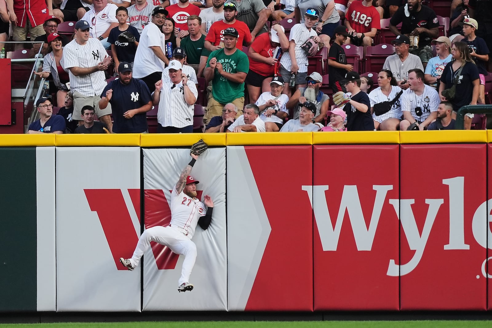 Cincinnati Reds right fielder Jake Fraley (27) falls into the wall after catching a fly ball hit by New York Yankees' Paul Goldschmidt during the fifth inning of a baseball game, Monday, June 23, 2025, in Cincinnati. (AP Photo/Joshua A. Bickel)