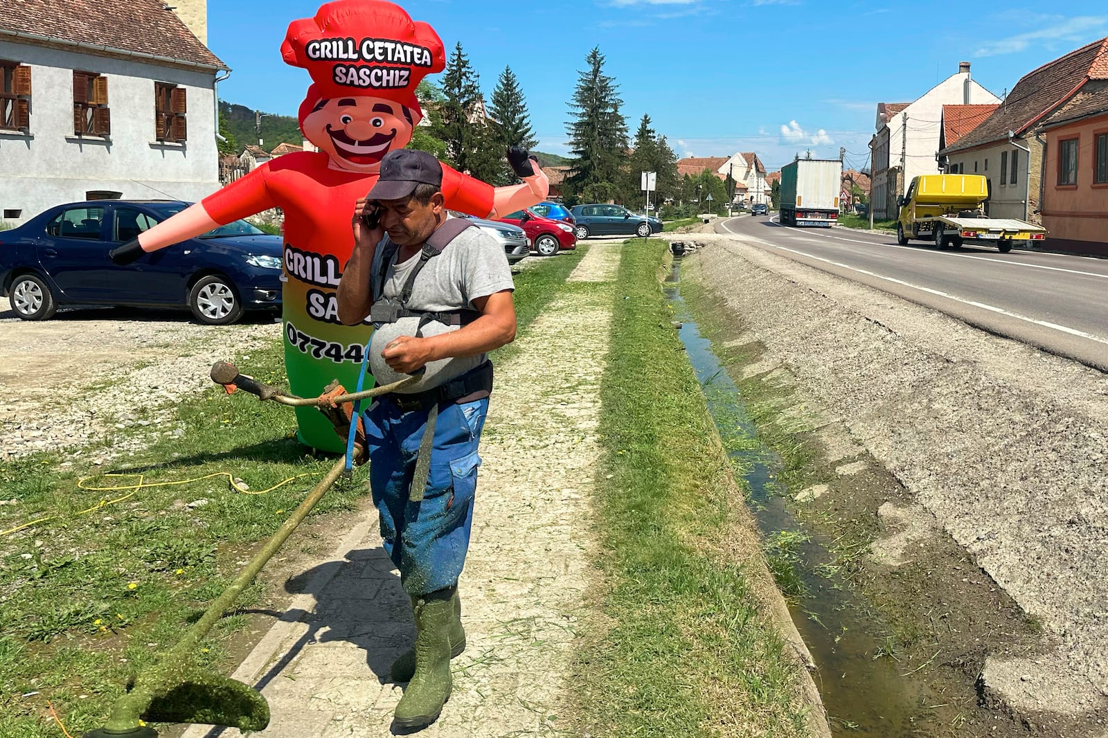 A man cuts grass in the village of Saschiz, in Romania's central Transylvania region, Friday, April 25, 2025. (AP Photo/Stephen McGrath)