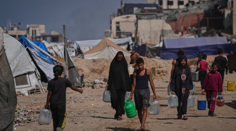 Palestinians carry jerrycans and plastic bottles with water after collecting it at a camp for displaced people in Gaza City, Thursday Oct. 23, 2025. (AP Photo/Abdel Kareem Hana)