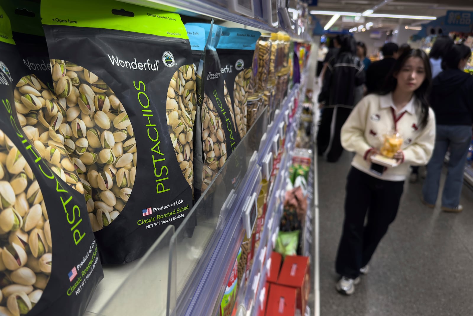 People walk by shelf displaying imported nuts from the United States, at the Hema supermarket, in Beijing, Tuesday, April 8, 2025. (AP Photo/Andy Wong)