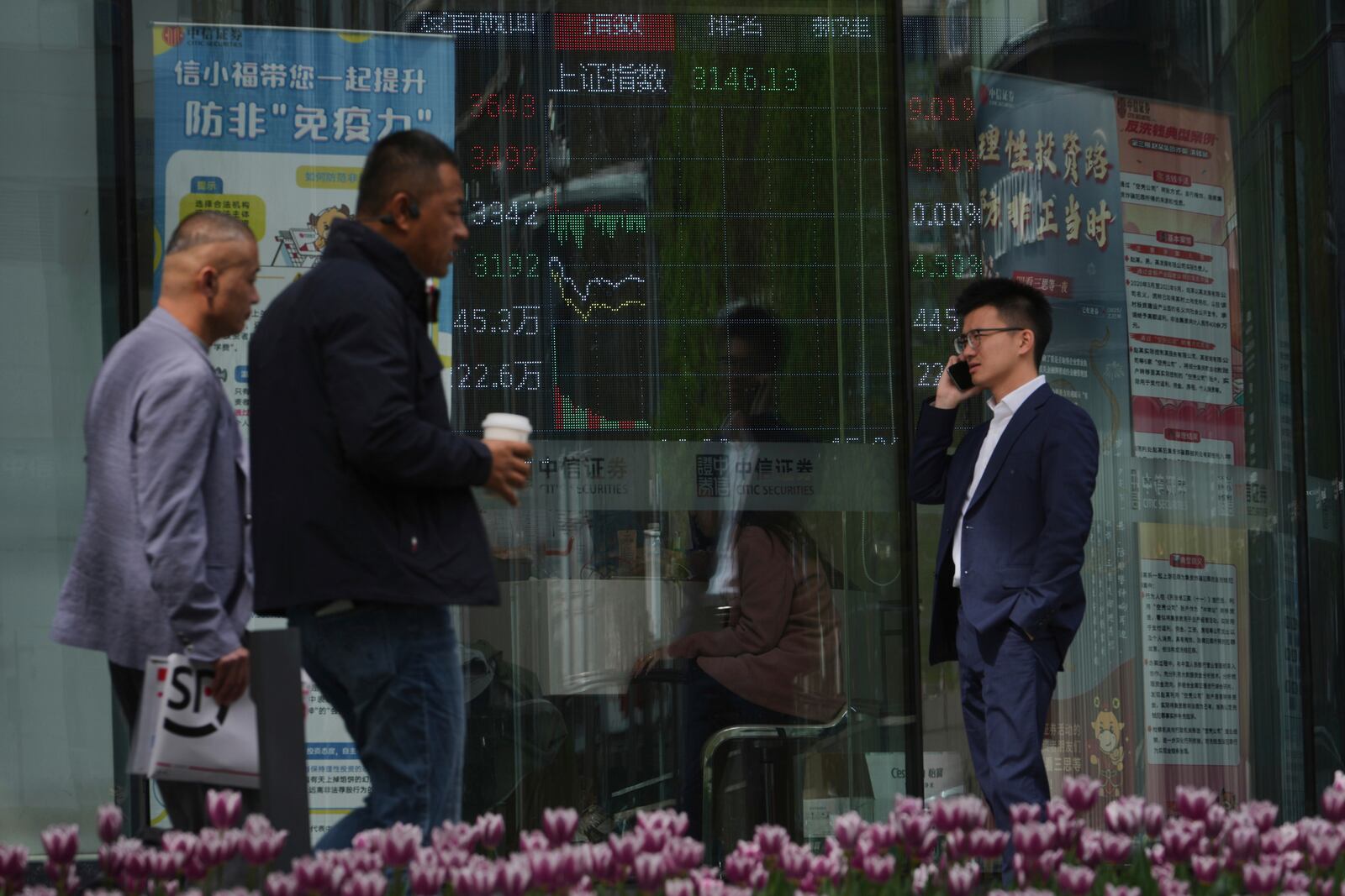 People walk by an electronic board displaying Shanghai shares trading index at a brokerage house, in Beijing, Monday, April 7, 2025. (AP Photo/Andy Wong)