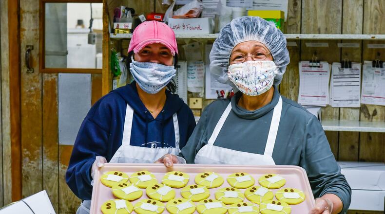 Alyssa Hyden, left, and owner Vera Slamka show off a tray of cookies with masks on them Monday, April 13, 2020 at Central Pastry in Middletown. Central Pastry has taken several steps to maintain safety of employees and customers. They are wearing face masks and gloves, have installed shields in front of the counters and have assigned spaces on the floor to keep customers spaced out during busy times in the shop. NICK GRAHAM / STAFF