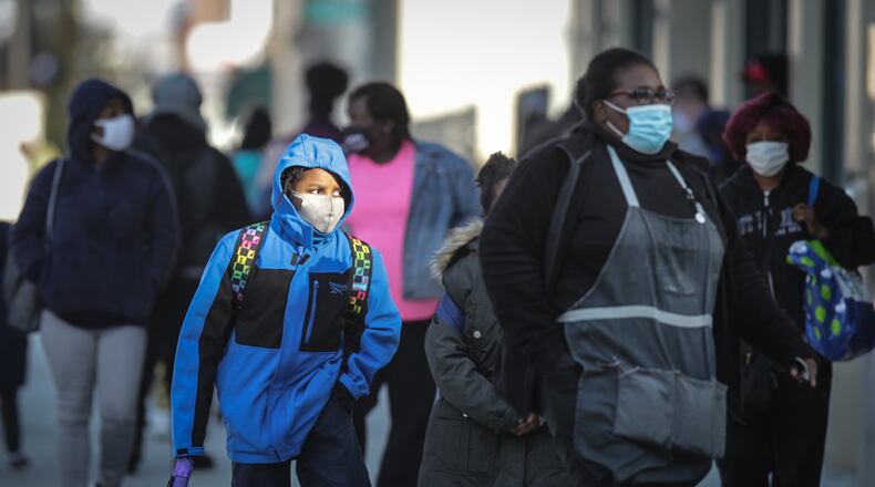Mostly mask wearing Pedestrians gather at Main and Third Streets in downtown Dayton to catch a bus.