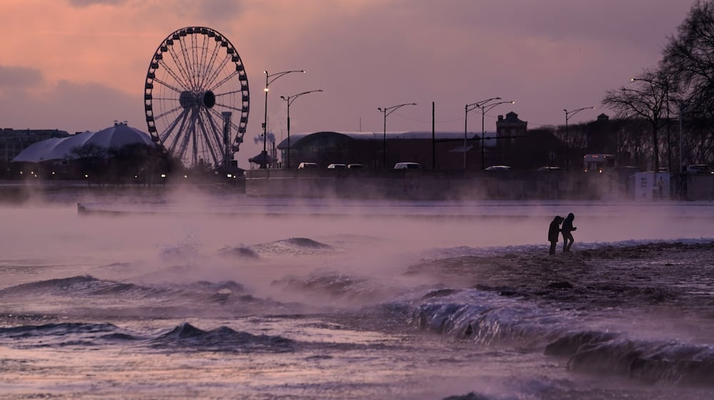 People walk on an ice covered beach along the shore of Lake Michigan, Friday, Jan. 23, 2026, in Chicago. (AP Photo/Kiichiro Sato)