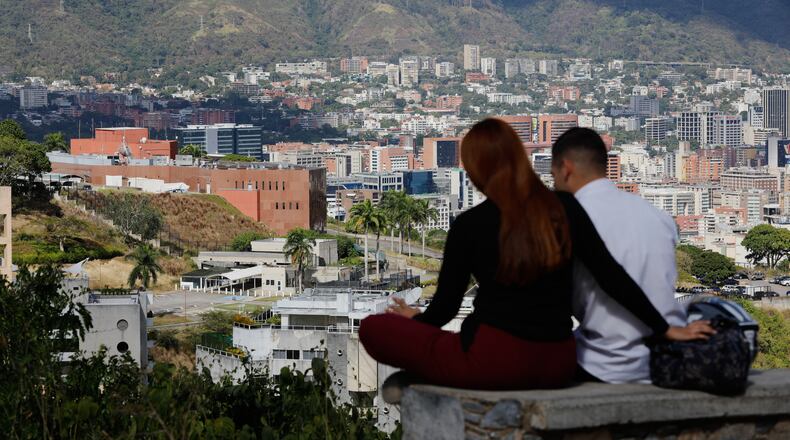 A couple sits on a bench at a viewpoint overlooking the U.S. embassy, center left, in Caracas, Venezuela, Friday, Jan. 9, 2026. (AP Photo/Cristian Hernandez)