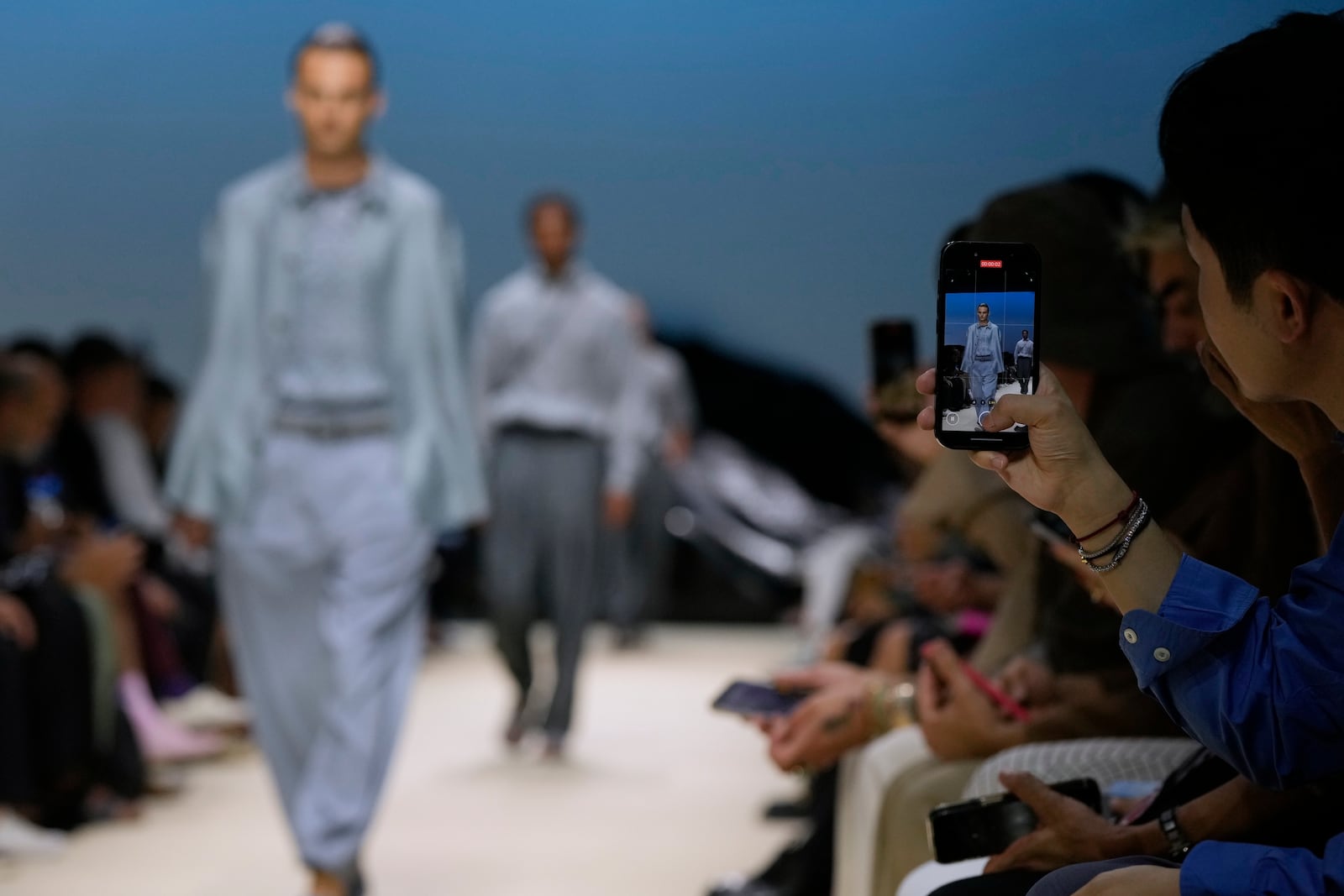 A guest takes a photograph during the men's Giorgio Armani Spring-Summer 2026 collection, that was presented in Milan, Italy, Monday, June 23, 2025. (AP Photo/Luca Bruno)