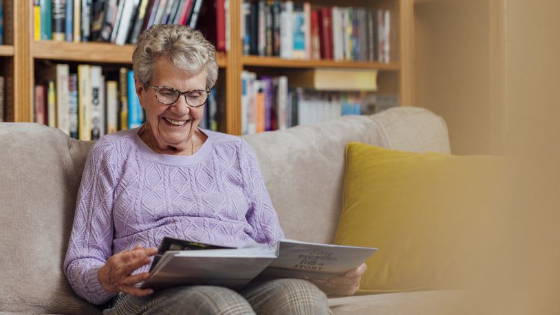 A senior woman with dementia looks through a photo album to aid her memory and remind her of the relationships she has with people in the book. iSTOCK/COX